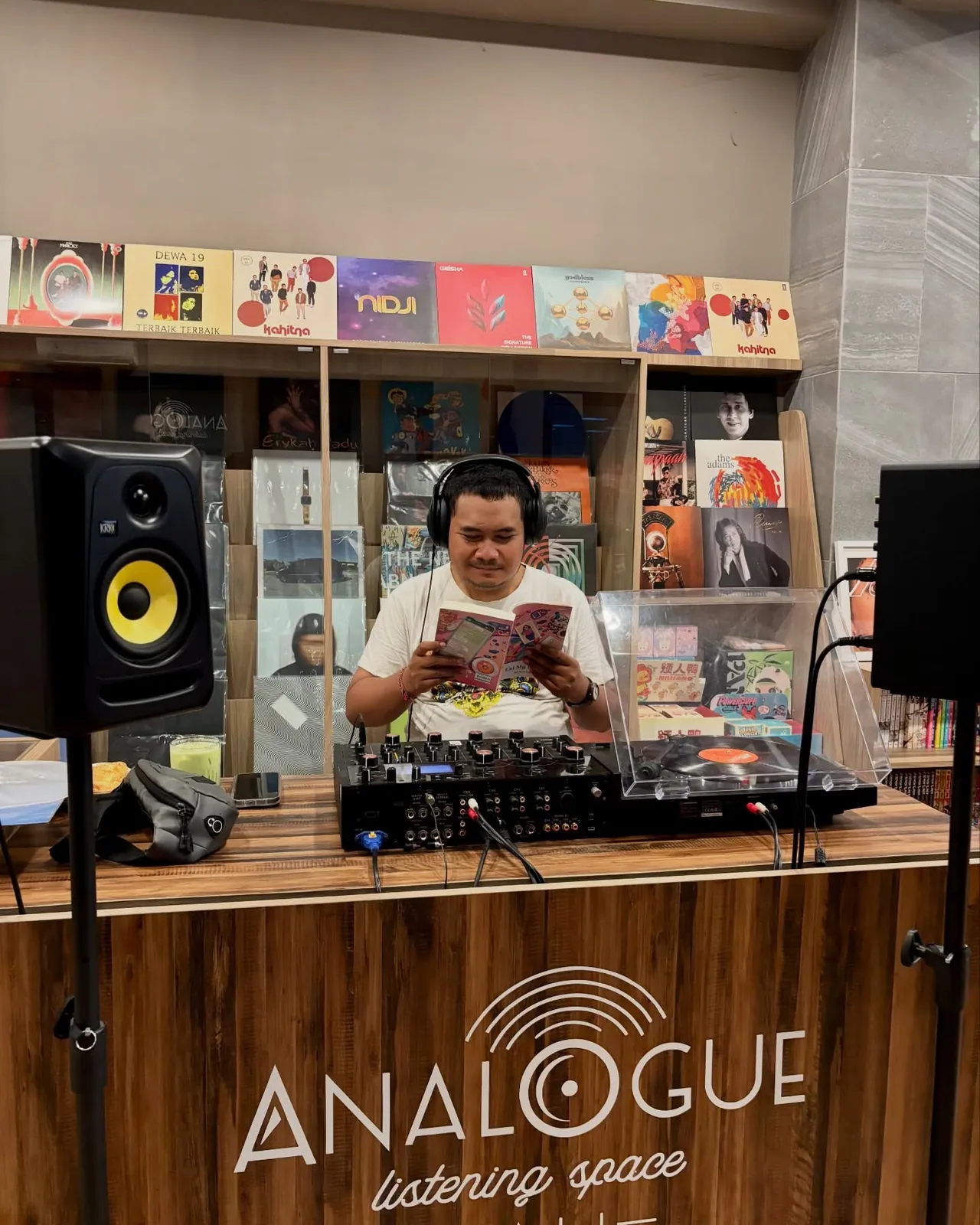 Peserta berheadphone membaca buku di balik meja DJ Analogue, dengan dinding sampul piringan hitam di belakangnya.